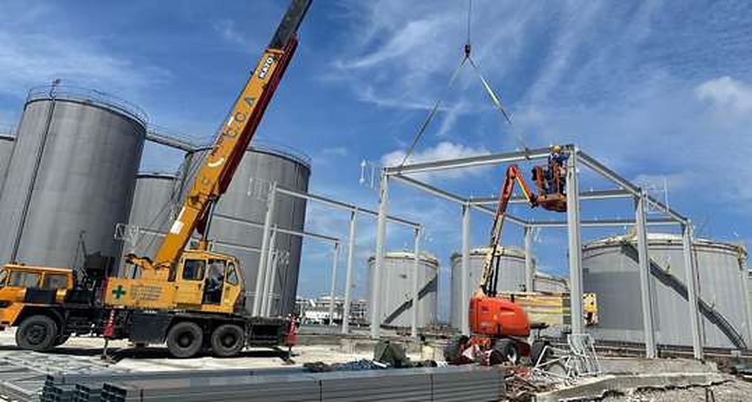 Steel frame erection beside storage tanks with crane and boom lifts
